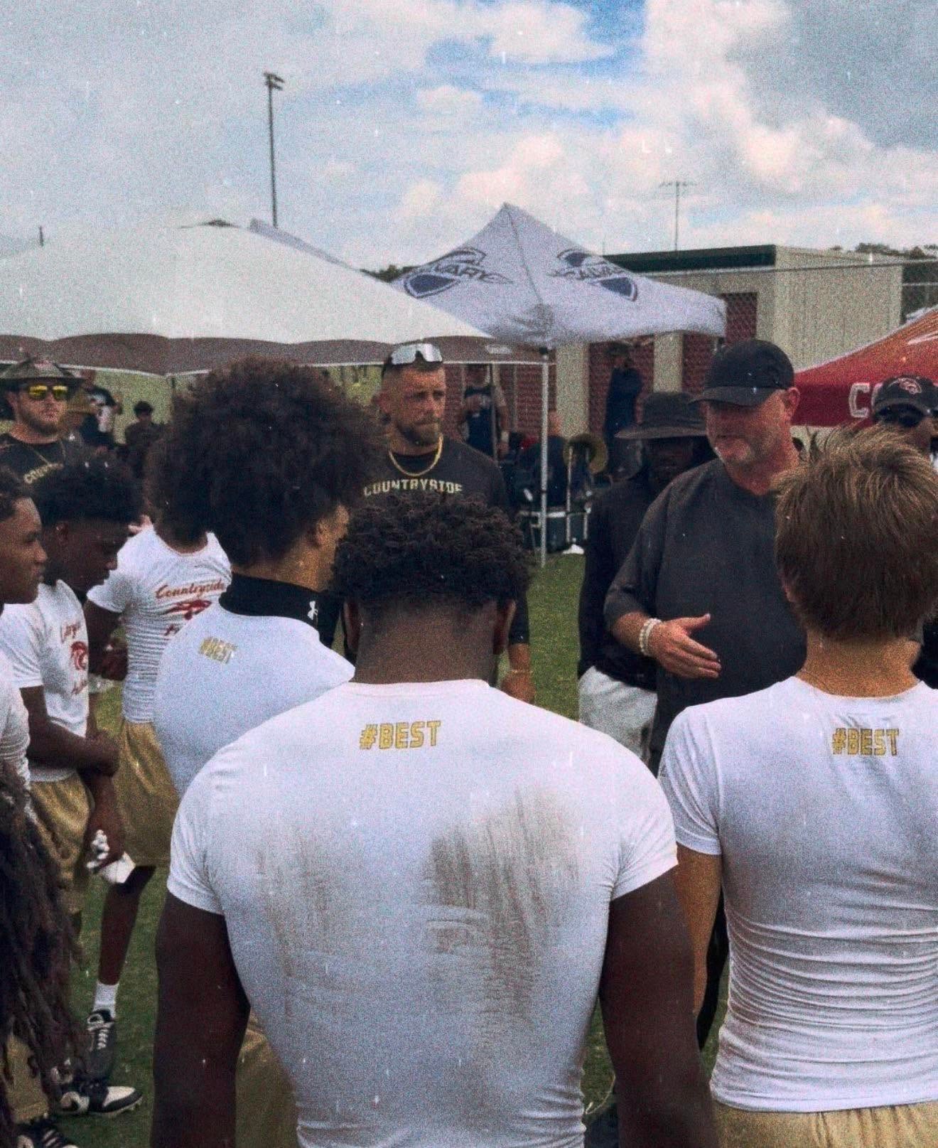 A coach addressing a group of young athletes at an outdoor event — mentorship and leadership development in action