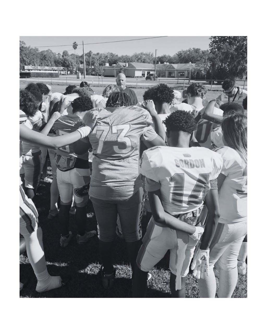 A coach leading a football team in a prayer circle — team culture, unity, and leadership through sport